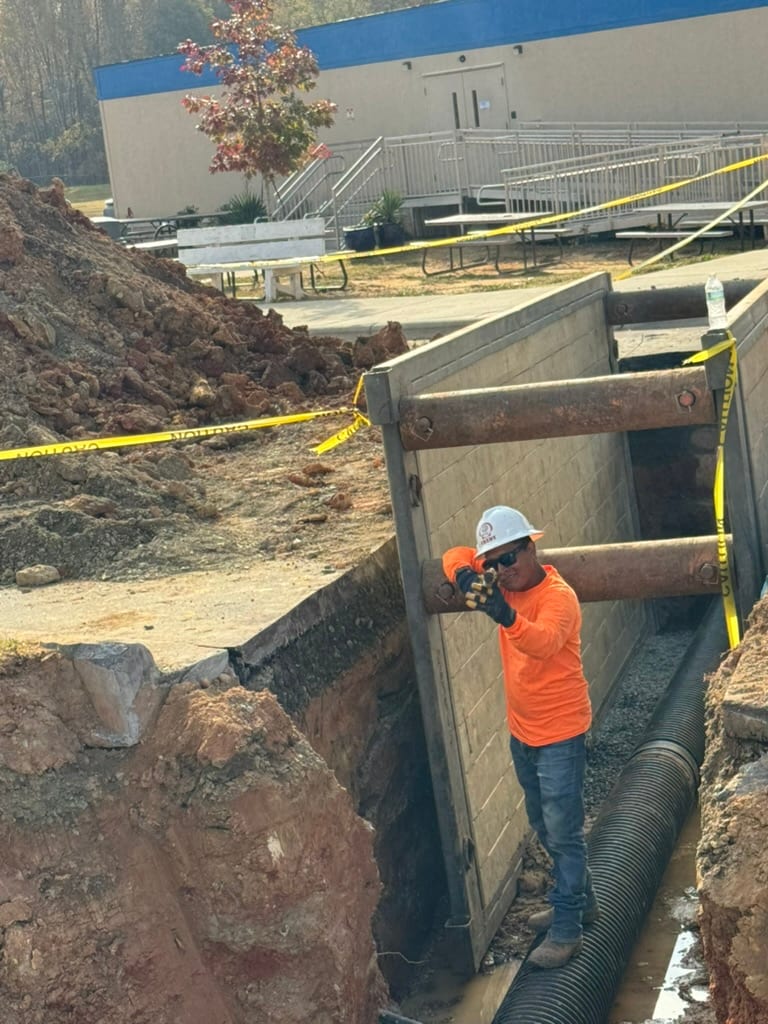 HD Grading crew member in hard hat and high-visibility gear working inside a shored utility trench