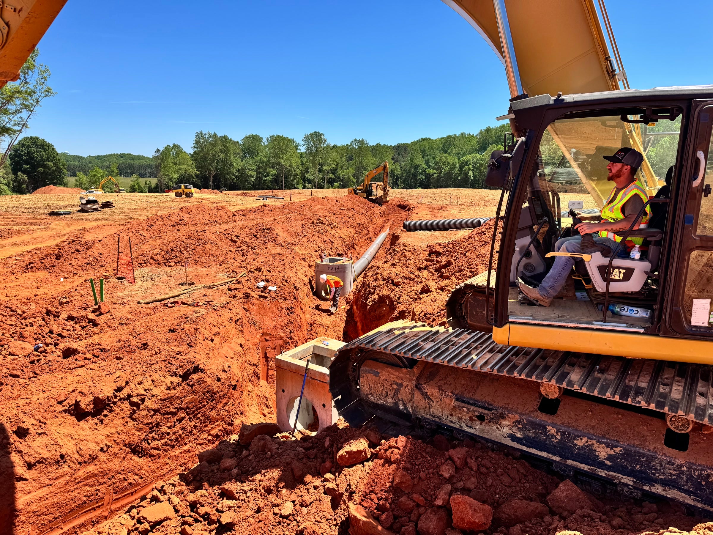 HD Grading operator in a CAT excavator working an active trench on a Carolinas job site